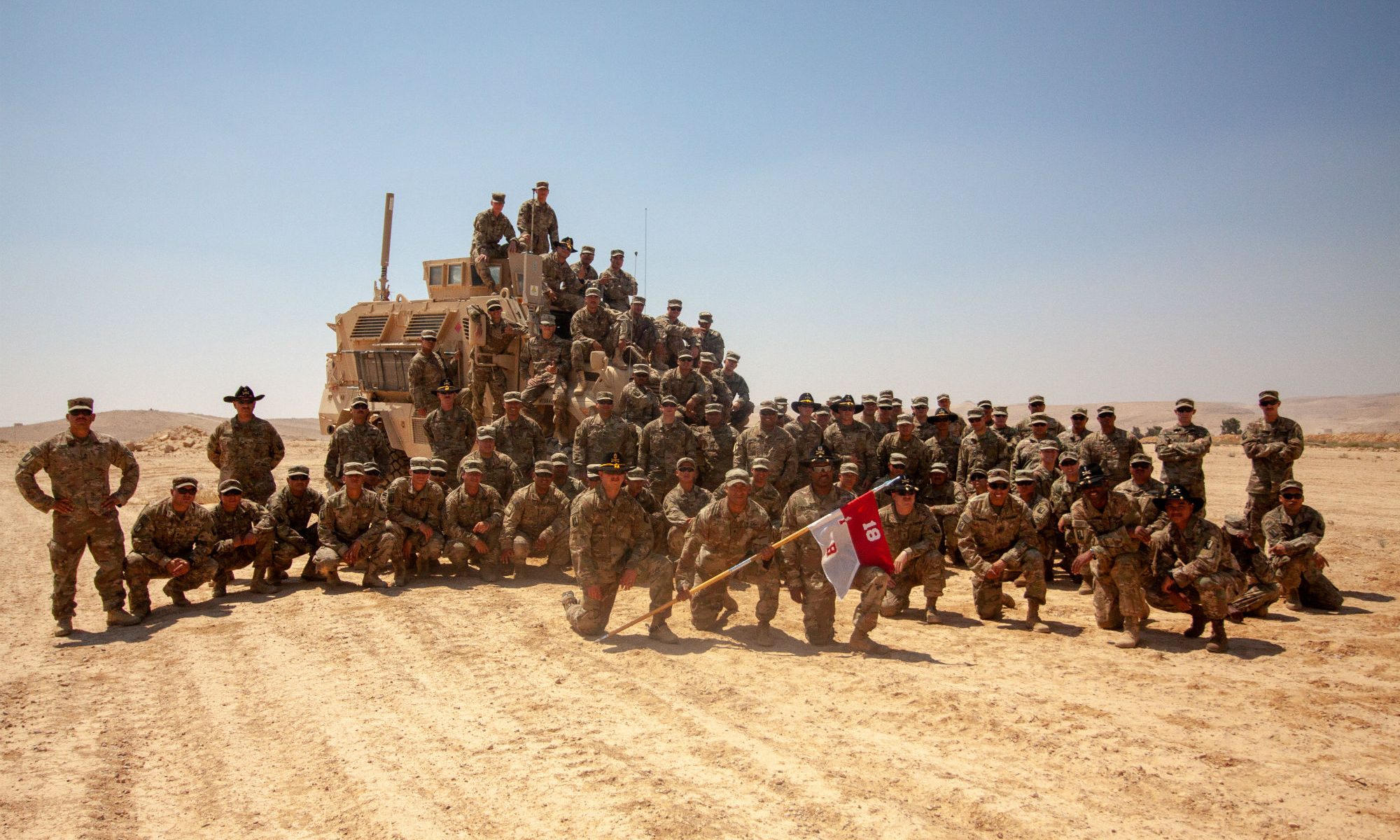 Large group of soldiers posing in a desert area with military vehicles.